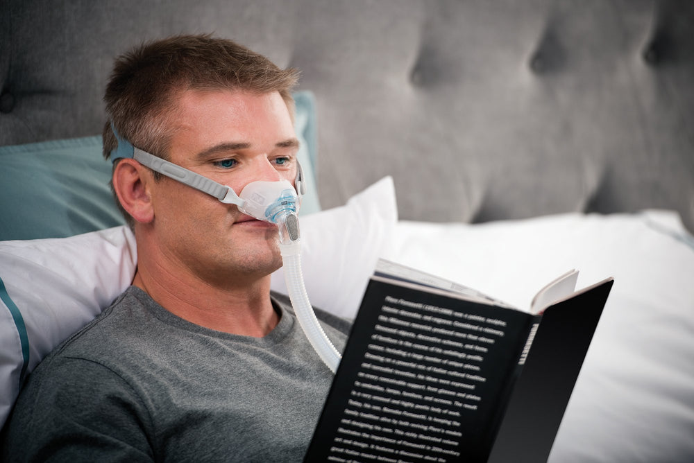 Man reading in bed wearing Brevida nasal pillows mask