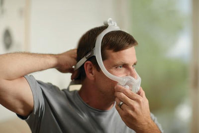Man putting on mask with headgear and full face cushion attached, side view
