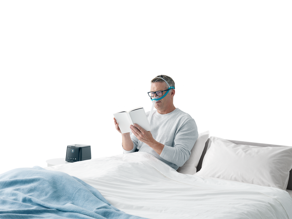 Man reading in bed wearing Evora mask with glasses on