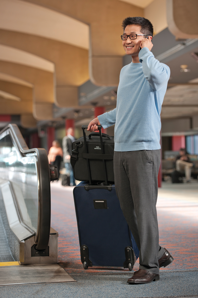 Man standing in airport with suitcase next to him with travel briefcase attached to suitcase